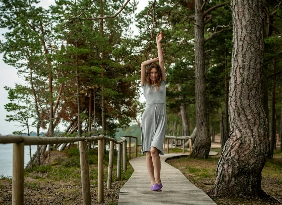 A woman stretching her arms to the sky on a wooden path between trees.